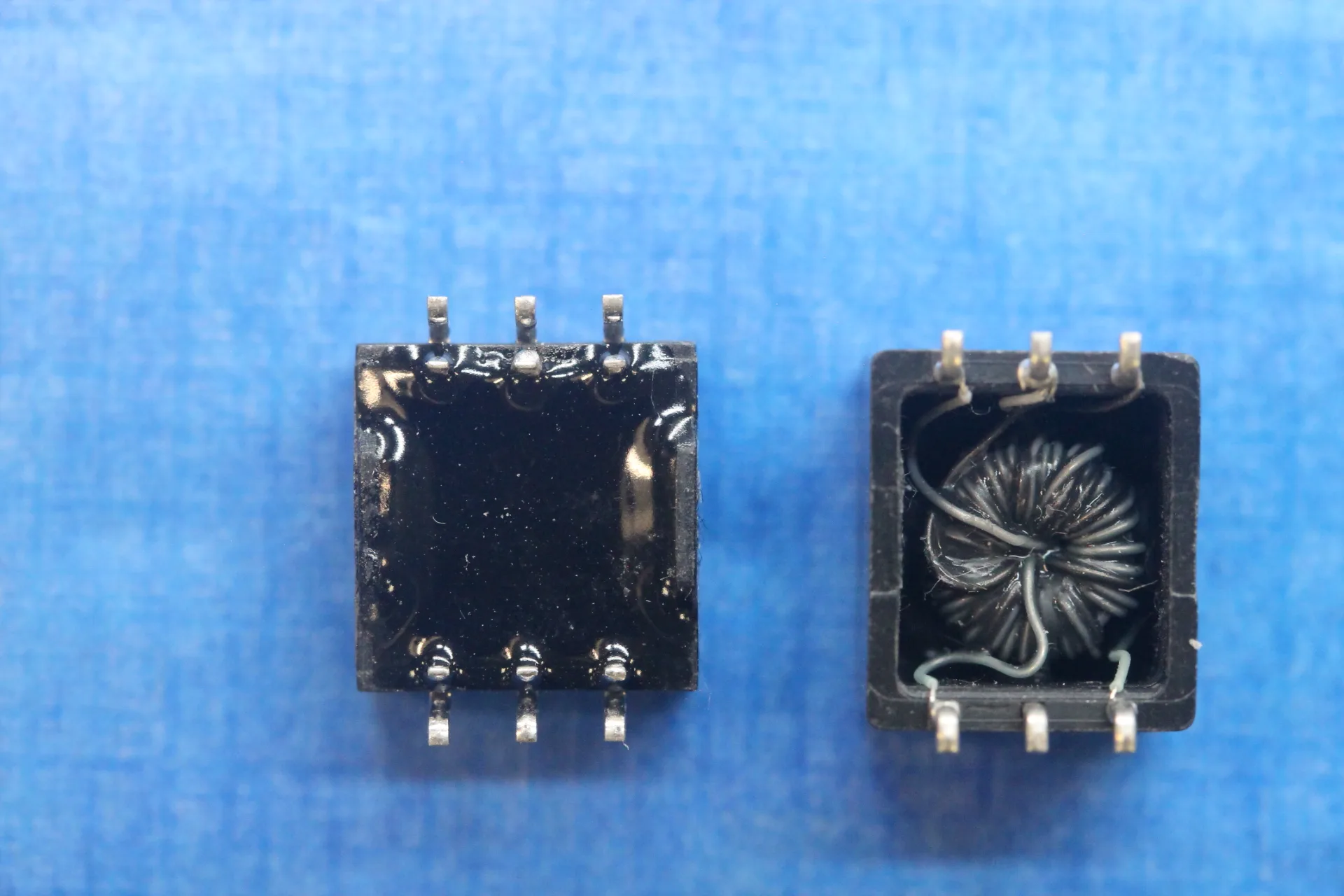 Two electronic components showing the underneath of the parts. One has been completely covered over, while the other shows a coil of wire.